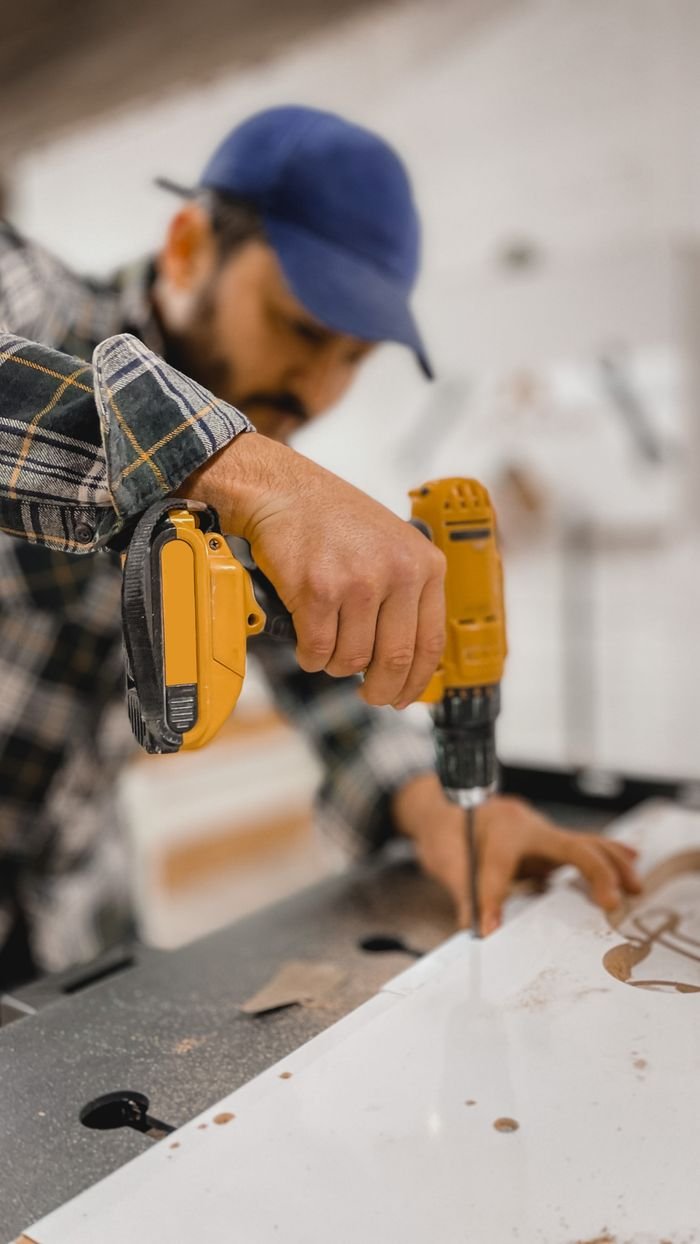 Close-up of a carpenter using a yellow drill in a workshop setting, focusing on hand.