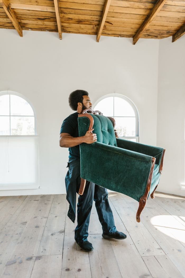 African American man carrying armchair in a bright, empty room, symbolizing moving day.
